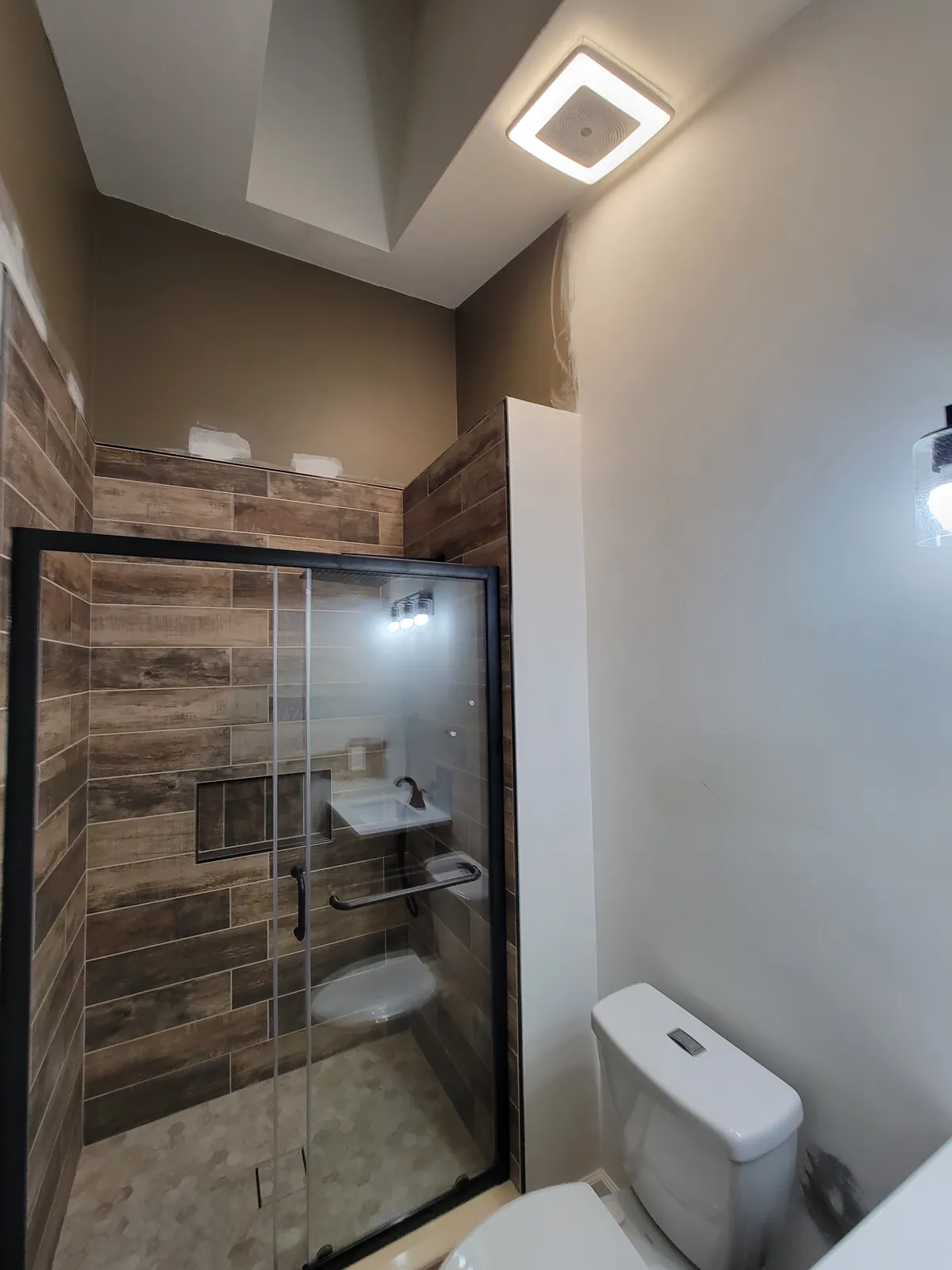 A Howell shower tiled in wood-look plank tile with a niche and glass door