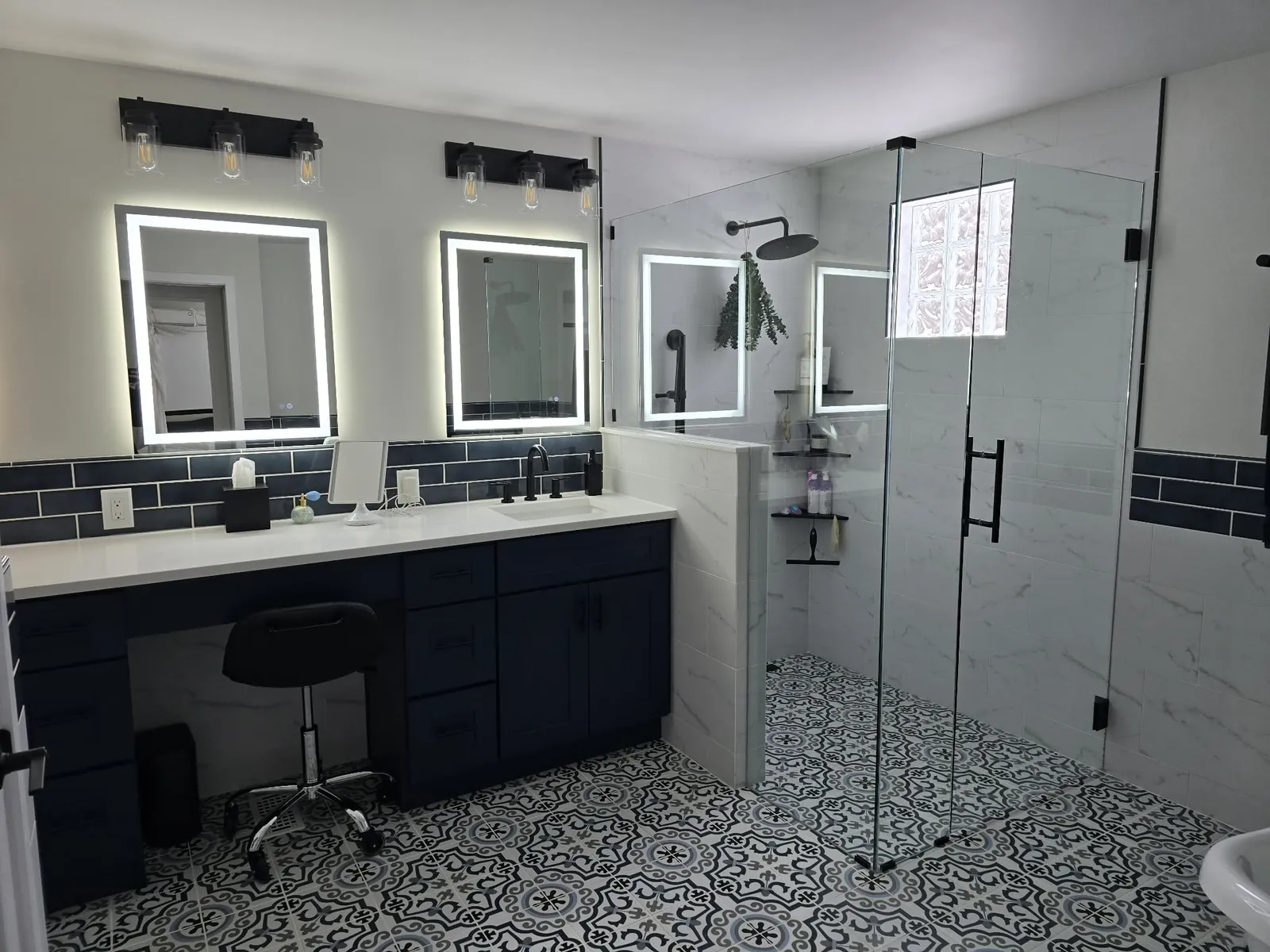 The finished Milford primary bathroom: navy double vanity with lit mirrors and patterned tile floor